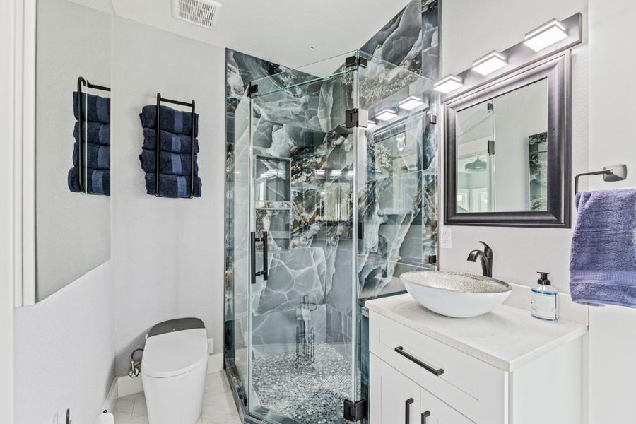 Glass-enclosed shower with custom stone-look paneling and pebble flooring