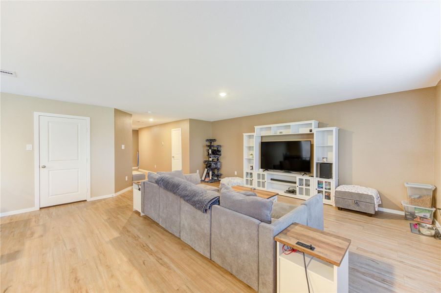 Spacious living room with wood flooring, featuring a large entertainment center and cozy sofa. Neutral walls and ample natural light create a warm, inviting atmosphere.