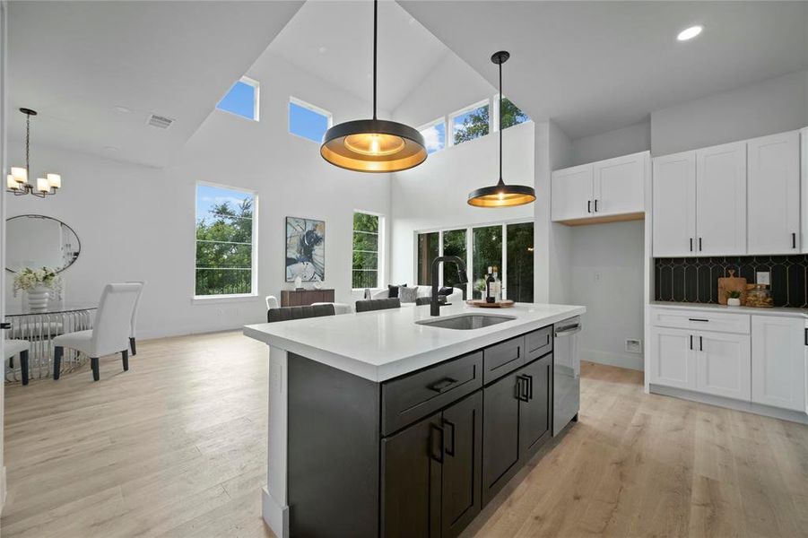 Kitchen featuring dishwasher, white cabinets, a towering ceiling, light countertops, and light wood finished floors Kitchen featuring dishwasher, white cabinets, a towering ceiling, light countertops, and light wood finished floors