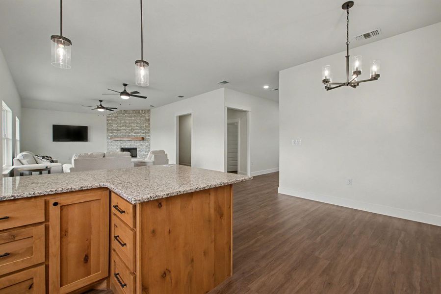 Kitchen featuring open floor plan, a fireplace, wood finish cabinetry, light stone counters, and dark wood-style flooring