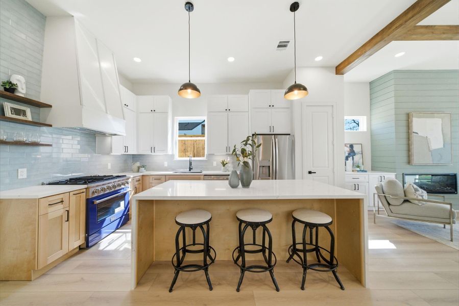 This photo showcases a modern, open-concept kitchen with sleek white cabinetry and light wood accents. It features a spacious island with seating, stainless steel appliances, and elegant pendant lighting.