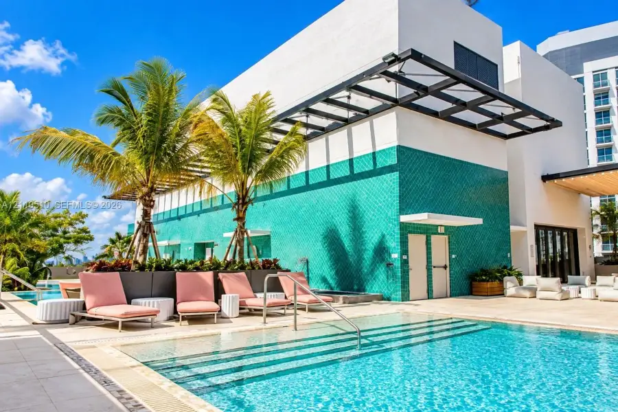 Swimming pool featuring tiered entry steps, teal geometric wall tiling, metal overhead structure, and stone-finish decking Swimming pool featuring tiered entry steps, teal geometric wall tiling, metal overhead structure, and stone-finish decking