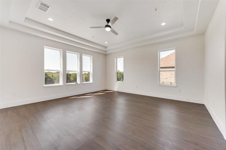 Expansive interior space featuring wood-finish flooring, a tiered tray ceiling, recessed lighting, and a modern ceiling fan Expansive interior space featuring wood-finish flooring, a tiered tray ceiling, recessed lighting, and a modern ceiling fan