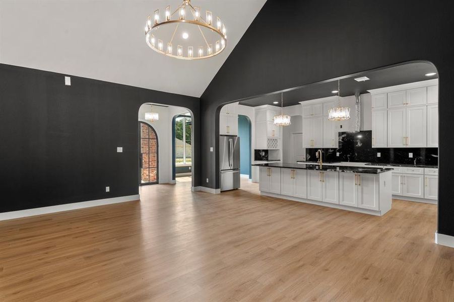 Kitchen with a chandelier, arched walkways, open floor plan, high vaulted ceiling, and white cabinetry