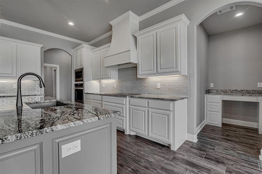 Kitchen with appliances with stainless steel finishes, custom exhaust hood, white cabinetry, and light stone counters