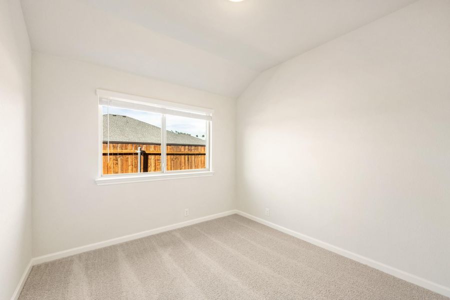 Empty bedroom with vaulted ceiling, carpet flooring, and single window with backyard view