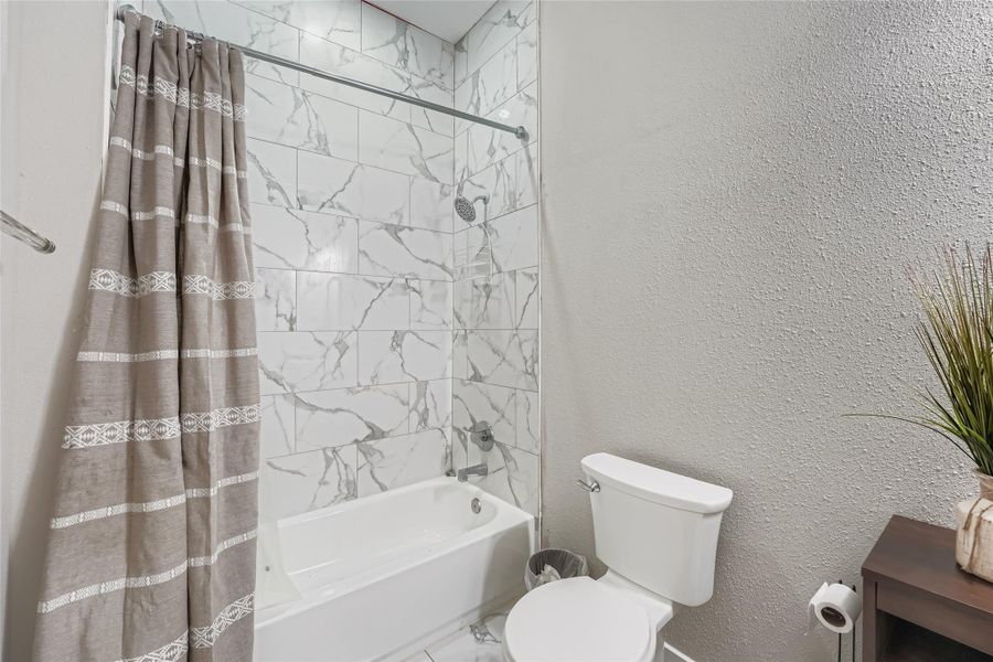 Bathroom featuring shower / bath combo and a textured wall Bathroom featuring shower / bath combo and a textured wall