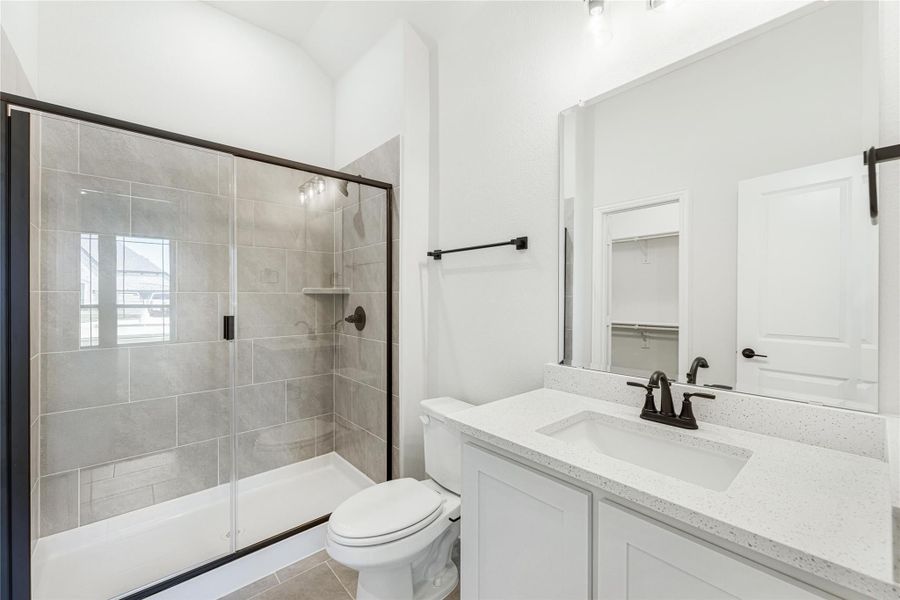 Bathroom with tiled shower and glass door, white vanity with quartz countertop, and toilet