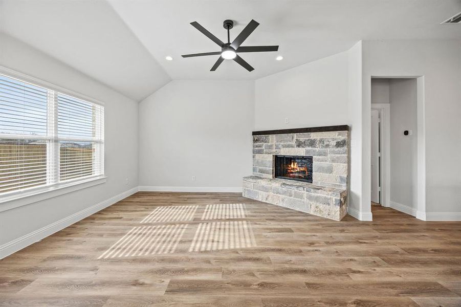 Unfurnished living room with a stone fireplace, light wood-style floors, recessed lighting, lofted ceiling, and a ceiling fan