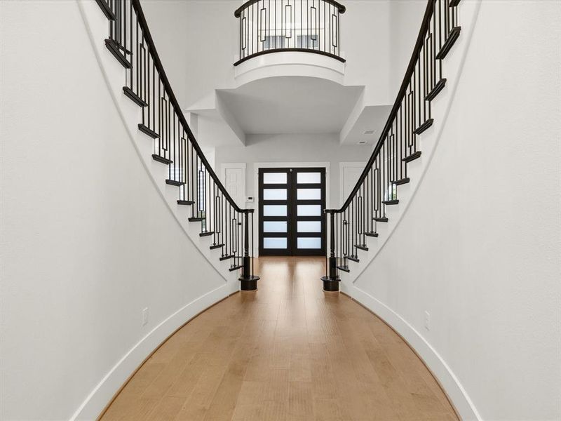 Grand entryway featuring a curved staircase with wrought iron balusters and a wood-finish flooring Grand entryway featuring a curved staircase with wrought iron balusters and a wood-finish flooring