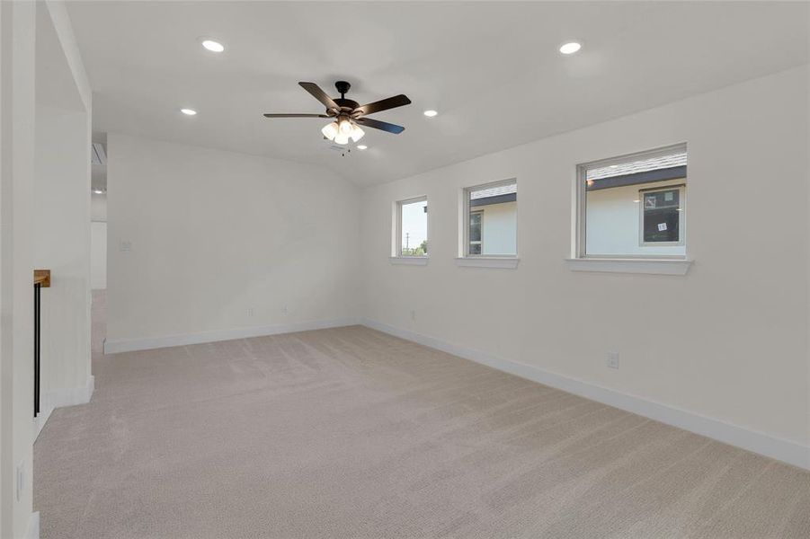 Spacious room featuring neutral carpeting, white walls, multiple recessed lights, a ceiling fan with integrated lighting, and three windows providing natural illumination