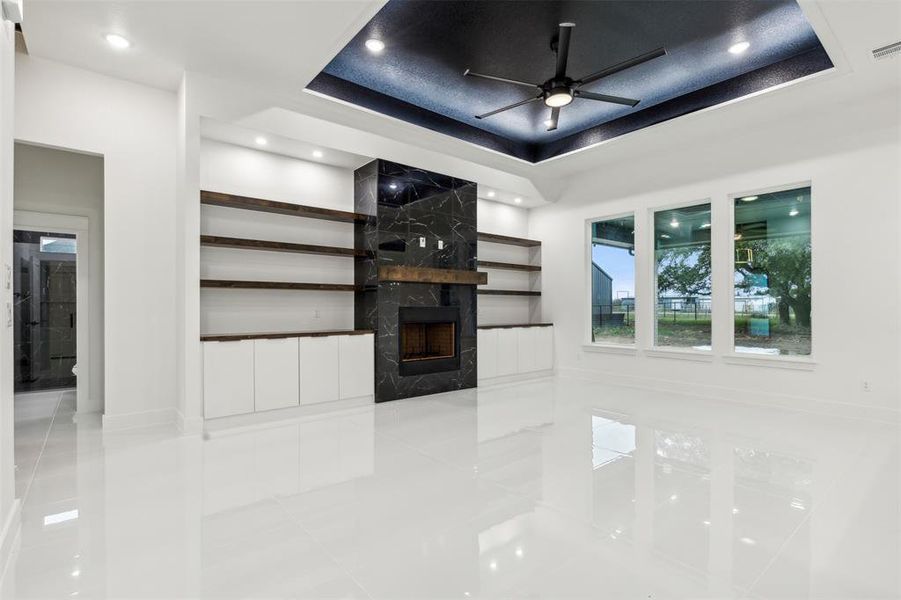 Unfurnished living room with ceiling fan, a high end fireplace, light tile patterned floors, and a raised ceiling