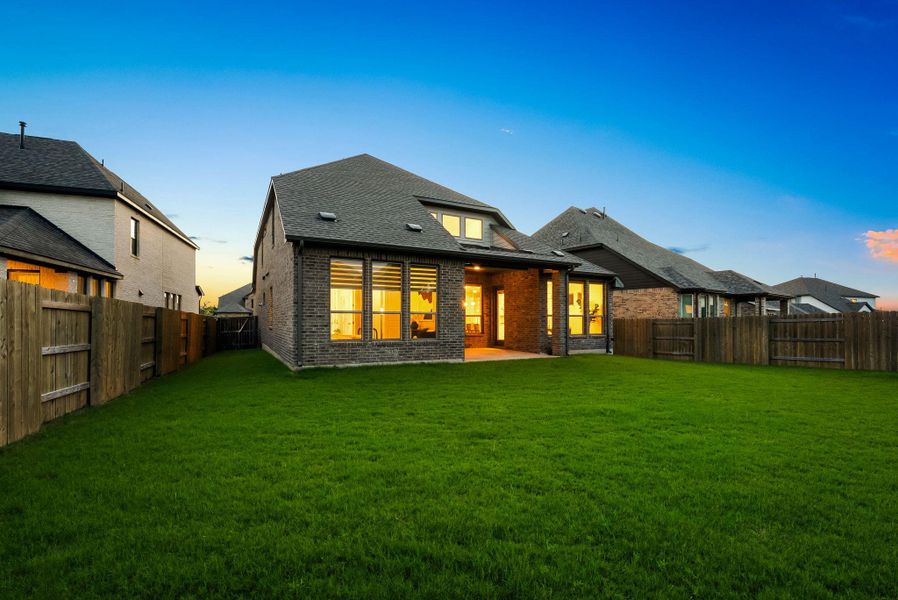 A deep green lawn surrounds the charming brick dwelling, illuminated by warm interior lighting at dusk.