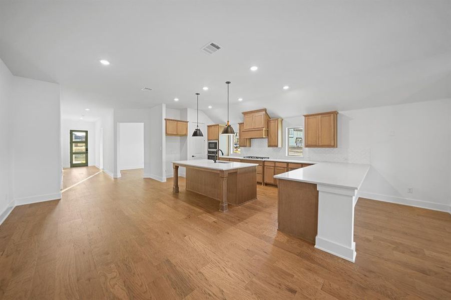 Kitchen featuring a breakfast bar, light countertops, a center island with sink, light wood-style flooring, and recessed lighting Kitchen featuring a breakfast bar, light countertops, a center island with sink, light wood-style flooring, and recessed lighting