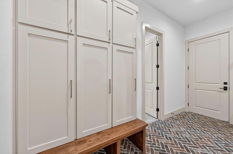 Built-in cabinetry with shaker-style doors and linear pulls, integrated wooden bench, and herringbone pattern brick flooring