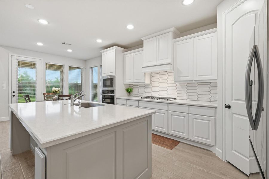 This modern kitchen features a spacious island with a sink, sleek stainless steel appliances, and ample white cabinetry. Natural light floods in through large windows, highlighting the stylish tile backsplash and open layout, perfect for cooking and entertaining. This modern kitchen features a spacious island with a sink, sleek stainless steel appliances, and ample white cabinetry. Natural light floods in through large windows, highlighting the stylish tile backsplash and open layout, perfect for cooking and entertaining.