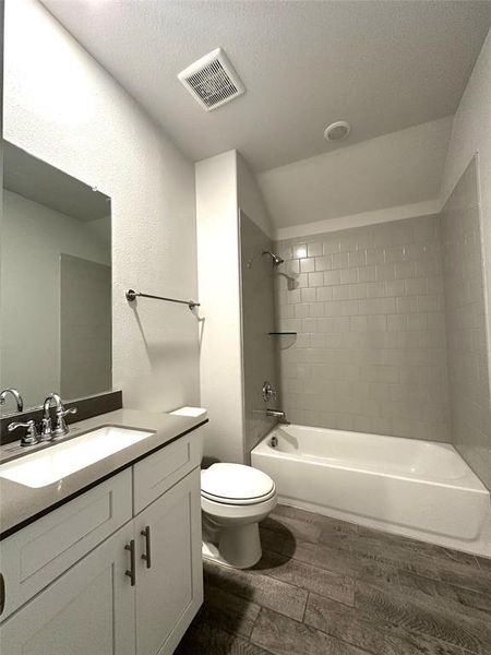 Full bathroom with hardwood / wood-style floors, vaulted ceiling, toilet, vanity, and tiled shower / bath combo