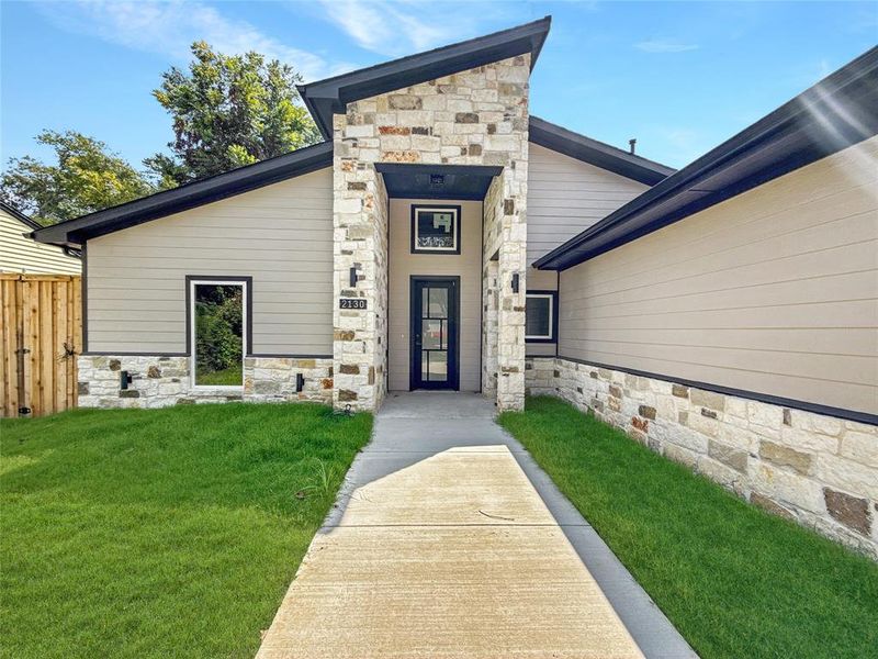 Entrance to property featuring stone siding and a yard