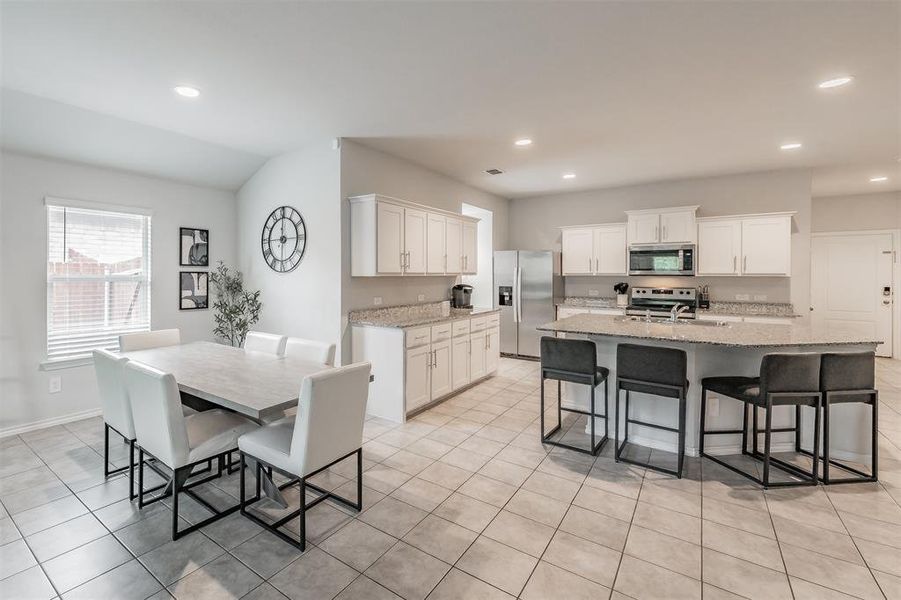 Open-concept kitchen and dining area featuring light-toned tile flooring, white cabinetry, granite countertops, stainless steel appliances, and recessed lighting