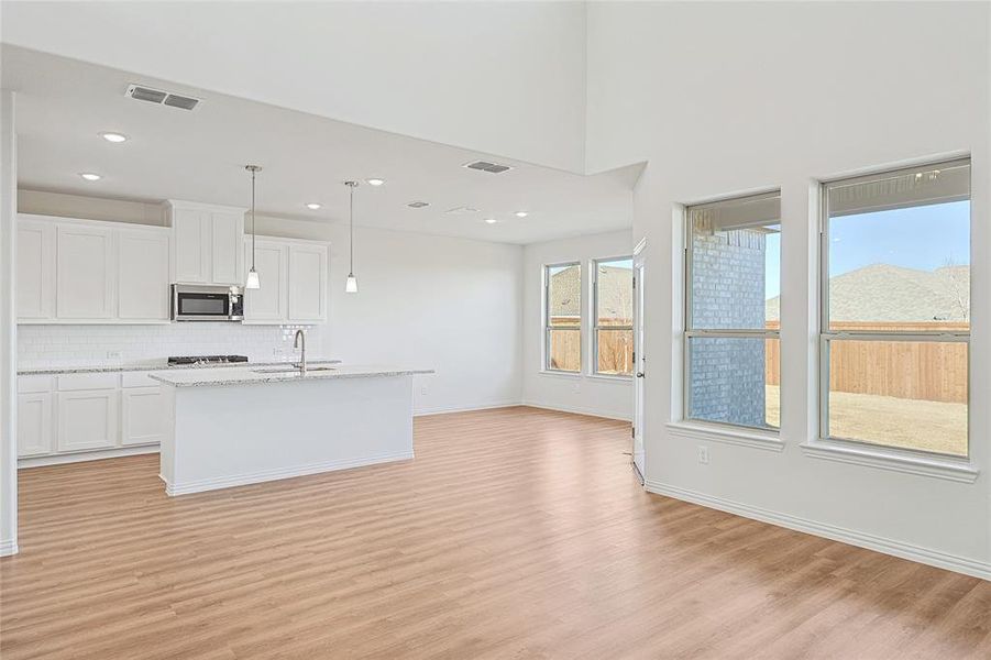 Kitchen featuring open floor plan, white cabinets, a center island with sink, decorative light fixtures, and light wood-type flooring
