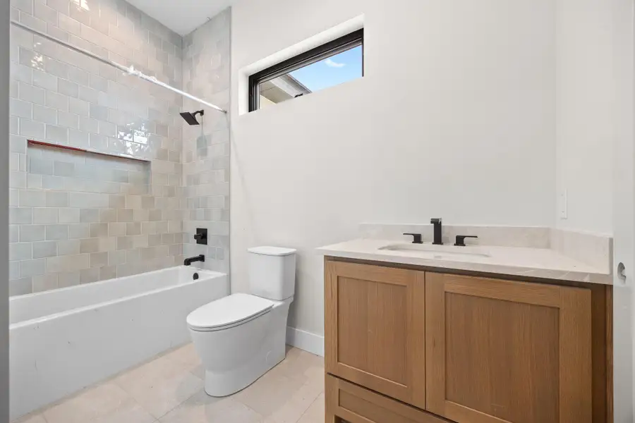 Bathroom featuring a white bathtub with subway tile surround, integrated shower niche, and matte black fixtures