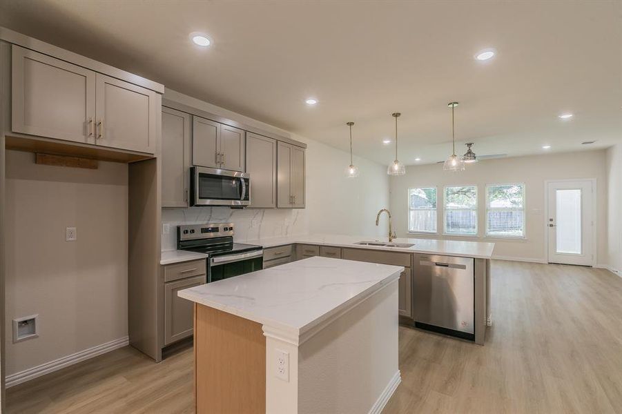 Kitchen featuring light stone countertops, appliances with stainless steel finishes, sink, decorative light fixtures, and a kitchen island