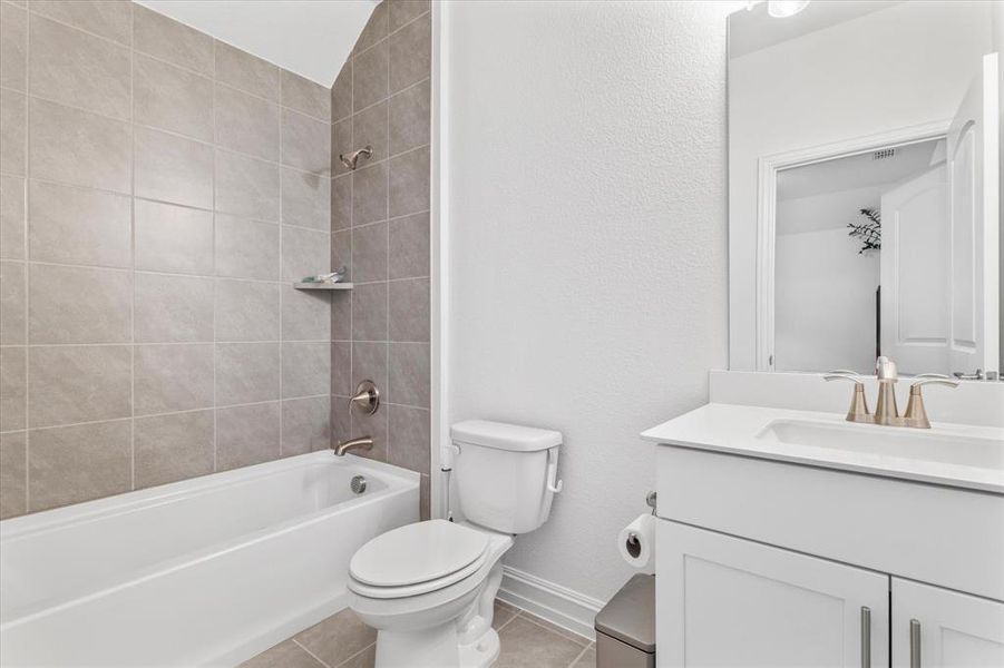 Full bathroom featuring a white bathtub with tile surround, a toilet, a vanity with a white countertop and integrated sink, and a large mirror