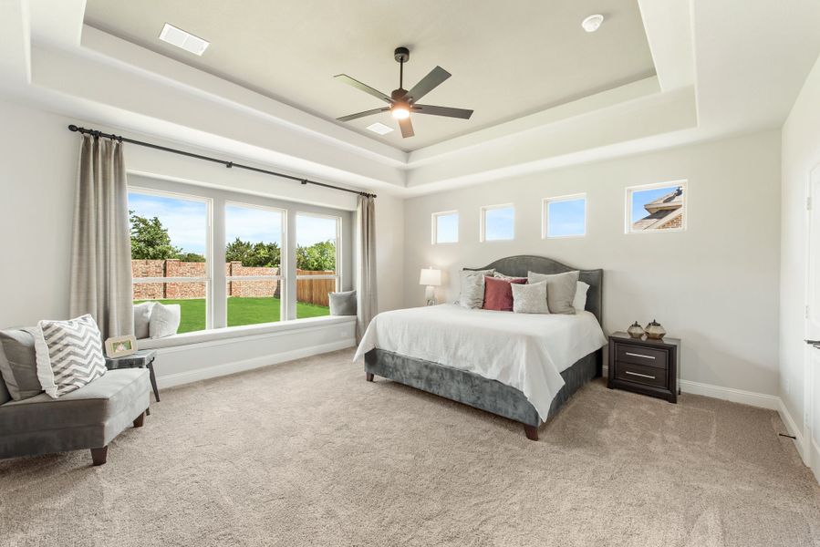 Master bedroom with tray ceiling, ceiling fan, window seat, and large windows overlooking backyard Master bedroom with tray ceiling, ceiling fan, window seat, and large windows overlooking backyard