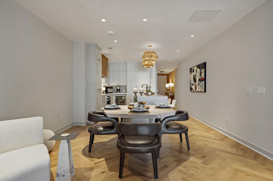 Herringbone hardwood floors extend through this open-concept dining area with an illuminated kitchen beyond.