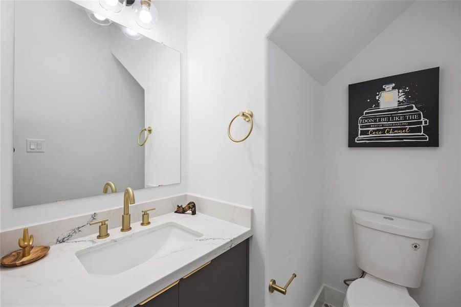 The powder room on the first floor is spacious. Brushed gold fixtures throughout highlight the modern aesthetic of the home.