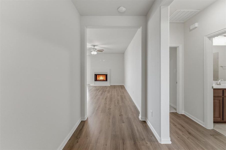 Hallway with wood-finish flooring extending into a living area featuring a fireplace with a white surround and a ceiling fan