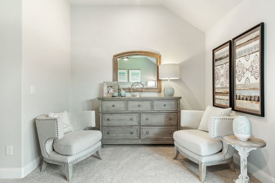 Bedroom sitting area with two white accent chairs, gray dresser with mirror, and vaulted ceiling
