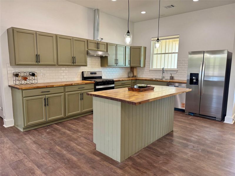 Kitchen with green cabinetry, stainless steel appliances, decorative light fixtures, decorative backsplash, and dark wood finished floors Kitchen with green cabinetry, stainless steel appliances, decorative light fixtures, decorative backsplash, and dark wood finished floors