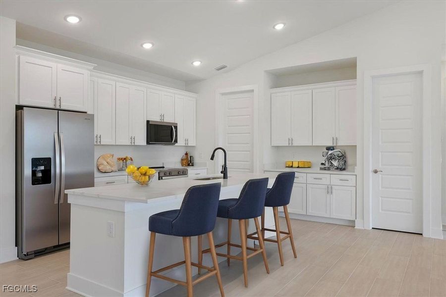 Kitchen with appliances with stainless steel finishes, vaulted ceiling, a kitchen breakfast bar, white cabinets, and recessed lighting