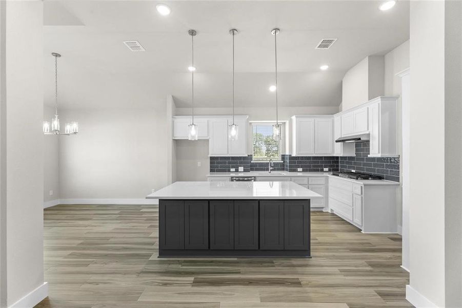Modern kitchen featuring an island with dark cabinetry and a light-toned countertop, white upper and lower perimeter cabinetry, a dark subway tile backsplash, and stainless steel appliances Modern kitchen featuring an island with dark cabinetry and a light-toned countertop, white upper and lower perimeter cabinetry, a dark subway tile backsplash, and stainless steel appliances