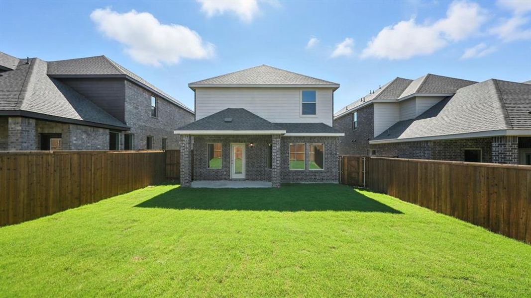 Rear view of house featuring brick siding, roof with shingles, a patio, and a fenced backyard