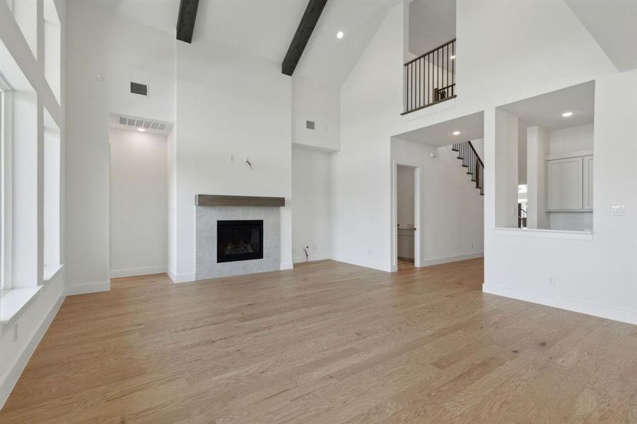 Vaulted ceiling with exposed wood beams, a fireplace with a stone surround and wood mantel, large windows, wood-finish flooring, and a second-story balcony with an iron railing Vaulted ceiling with exposed wood beams, a fireplace with a stone surround and wood mantel, large windows, wood-finish flooring, and a second-story balcony with an iron railing