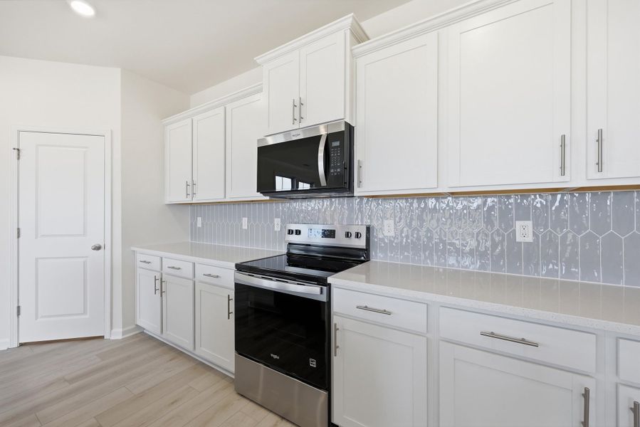 Kitchen featuring stainless steel appliances, white cabinetry, light stone counters, light wood-style floors, and decorative backsplash