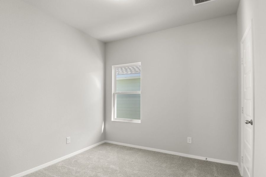 Image of a bedroom with tan carpeting, light grey walls and a window