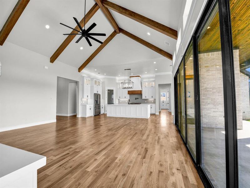 Unfurnished living room featuring light hardwood / wood-style floors, beam ceiling, high vaulted ceiling, and ceiling fan with notable chandelier