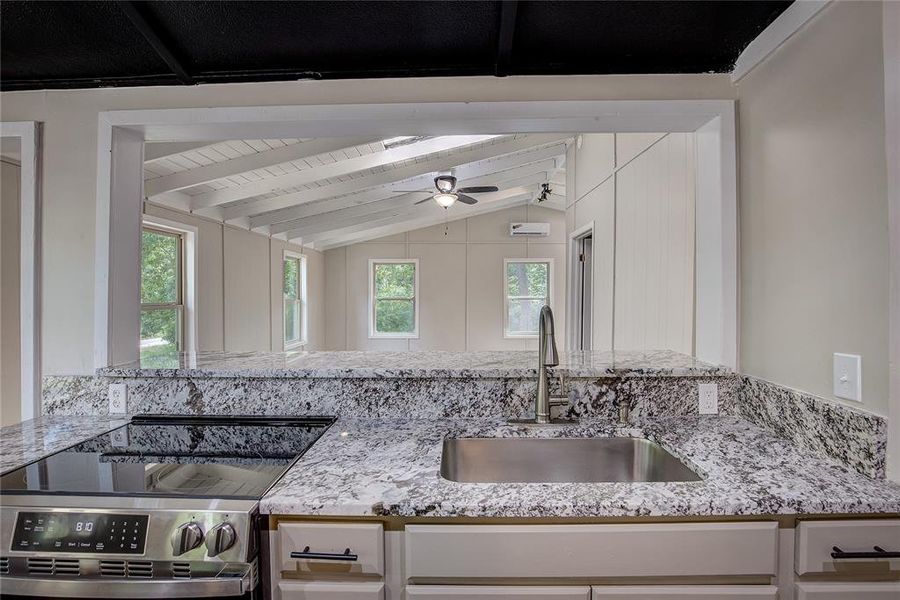 Kitchen featuring sink, white cabinetry, vaulted ceiling with beams, light stone counters, and stainless steel electric stove