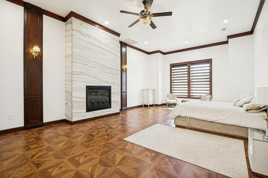 Spacious Primary Bedroom with patterned wood-finish flooring, wood trim, fireplace, seating area, decorate lighting \