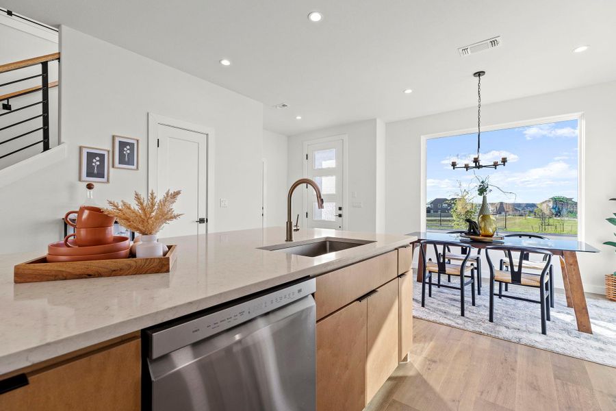 Kitchen featuring dishwasher, light stone countertops, light wood-style flooring, hanging lights, and a peninsula