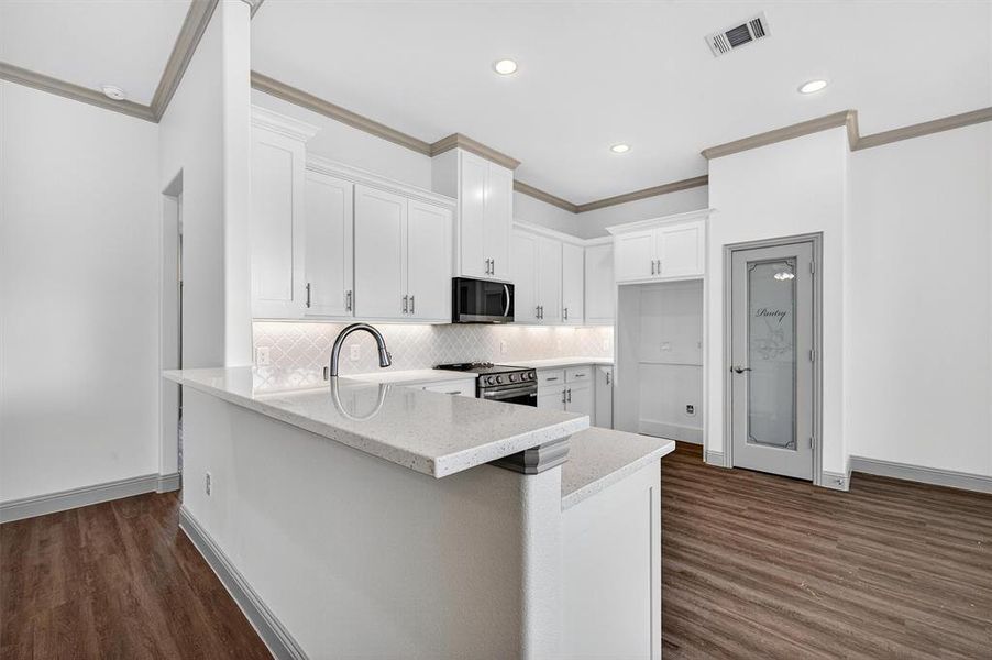 Kitchen with a peninsula, white cabinets, dark wood-style flooring, light stone countertops, and ornamental molding