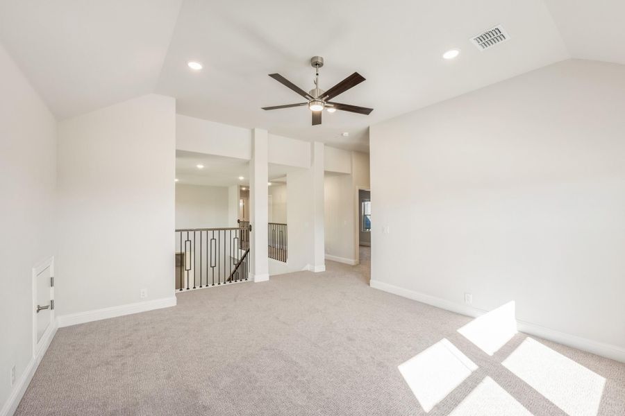 Open upstairs living area with gray carpet, ceiling fan, and metal stair railing overlooking lower level Open upstairs living area with gray carpet, ceiling fan, and metal stair railing overlooking lower level