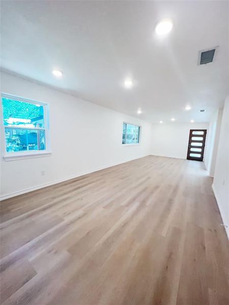Spacious room featuring wood-finish flooring, white walls, and multiple recessed ceiling lights