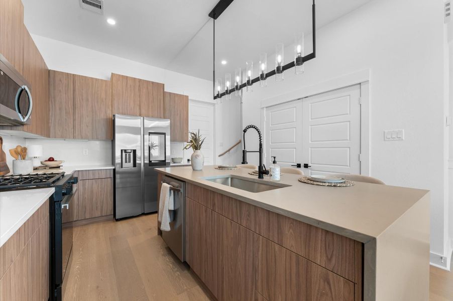 The kitchen, the heart of the second-floor open-concept living, dining, and kitchen, features a spacious island with a one-sided cascade quartz countertop, farmhouse sink, and modern pendant lights, complemented by an abundance of sleek, modern cabinetry providing ample storage, perfect for meal prep, casual breakfasts, or gathering with family and friends.