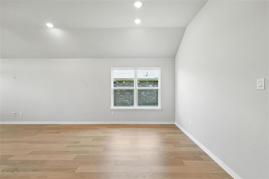 Empty room with lofted ceiling, light wood-style flooring, and recessed lighting Empty room with lofted ceiling, light wood-style flooring, and recessed lighting