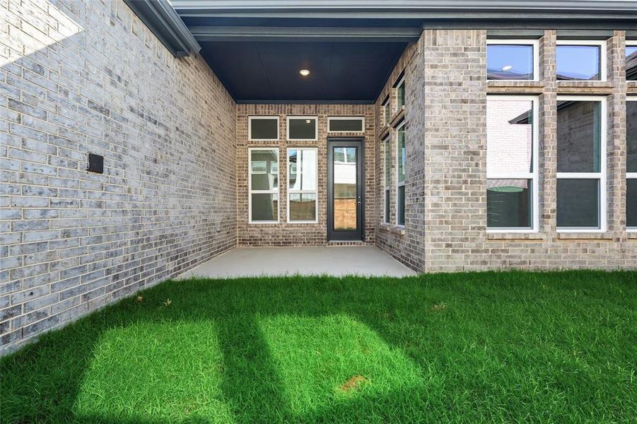 View of exterior entry featuring a yard, a patio, and brick siding