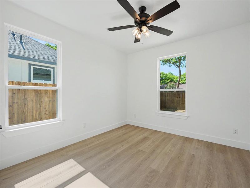 Room featuring wood-finish flooring, white walls, and a ceiling fan with light fixture Room featuring wood-finish flooring, white walls, and a ceiling fan with light fixture